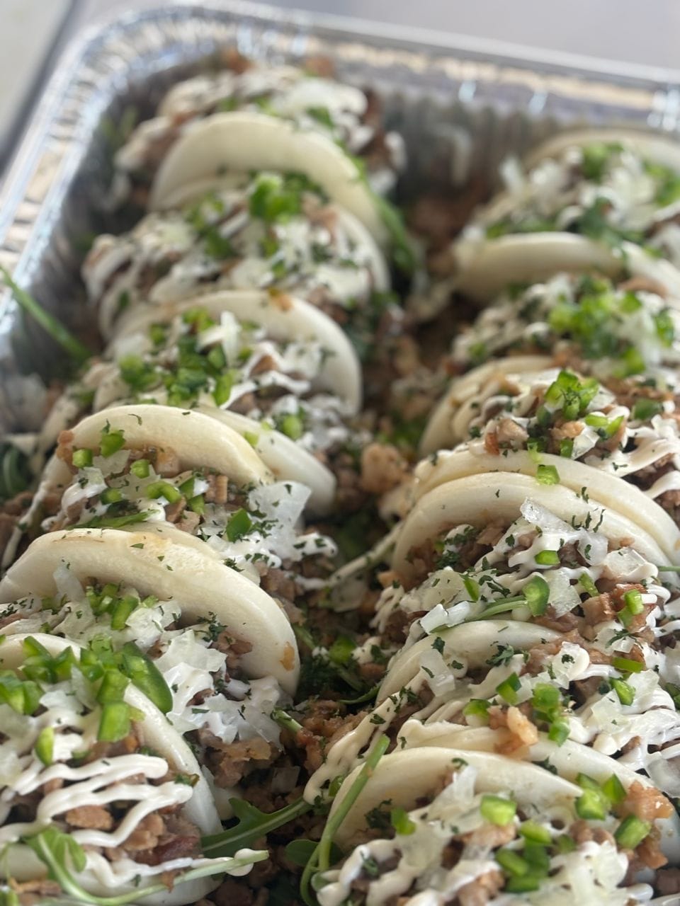 A catering pan of Shaka's bao buns with pork, green onion and sauce