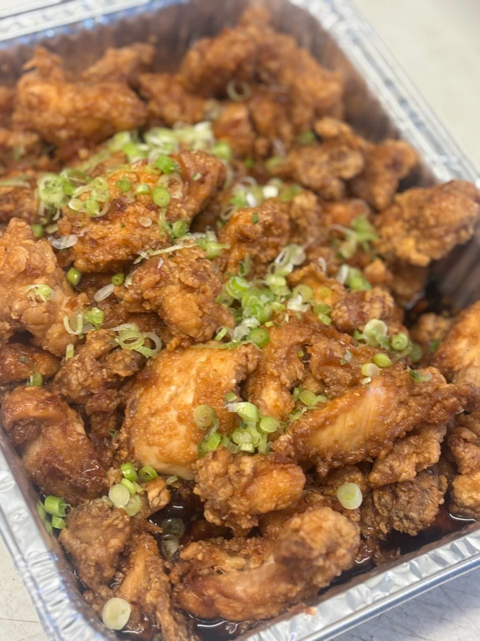 A catering pan of fried garlic chicken topped with green onion
