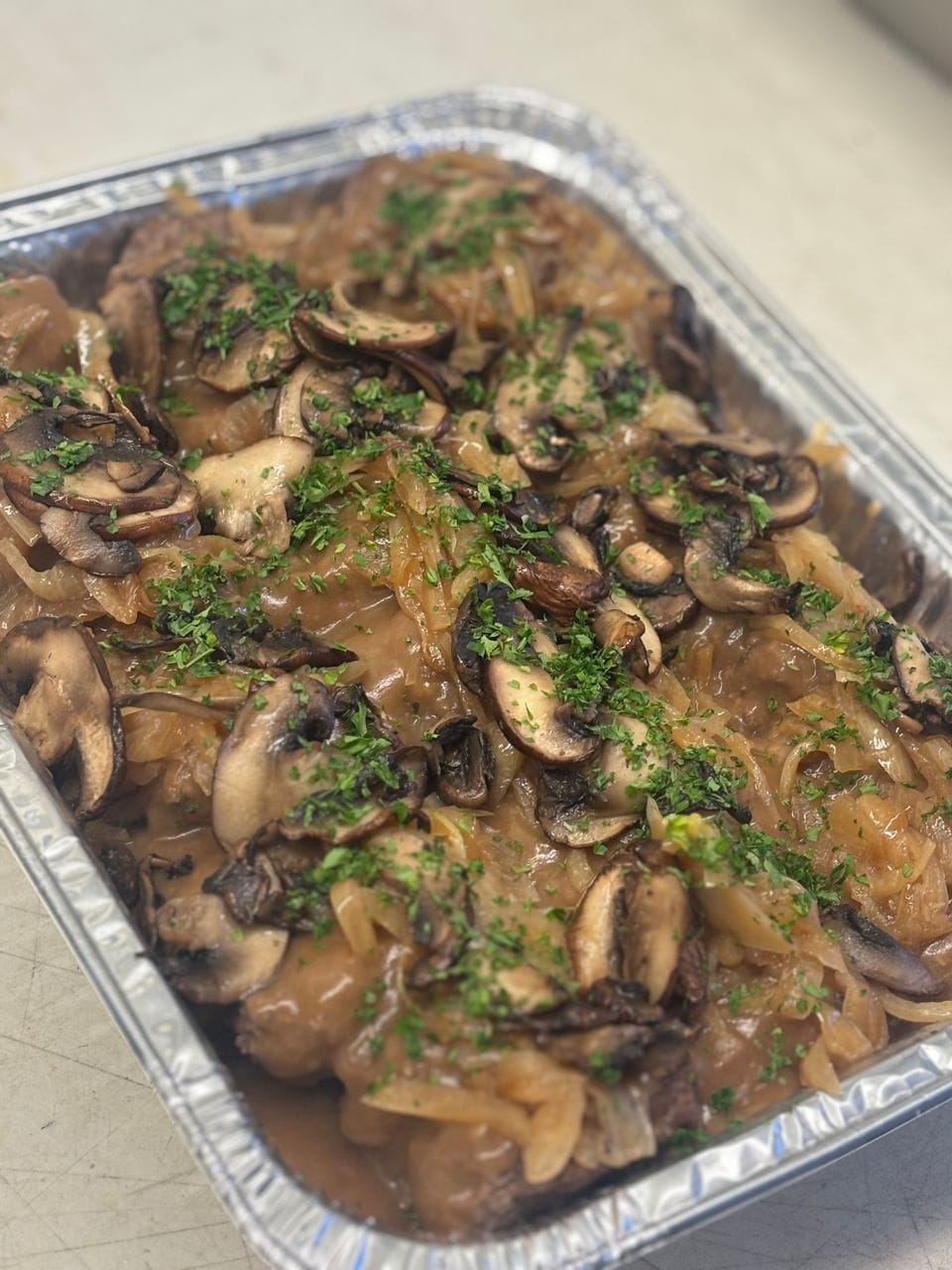 A catering pan of hamburger steak with mushroom gravy