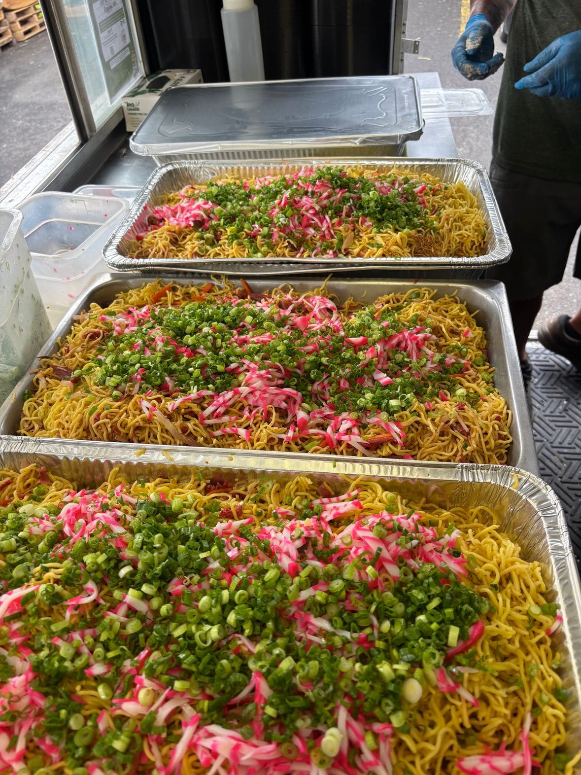 Catering pans of fried noodles topped with green onion and fishcake