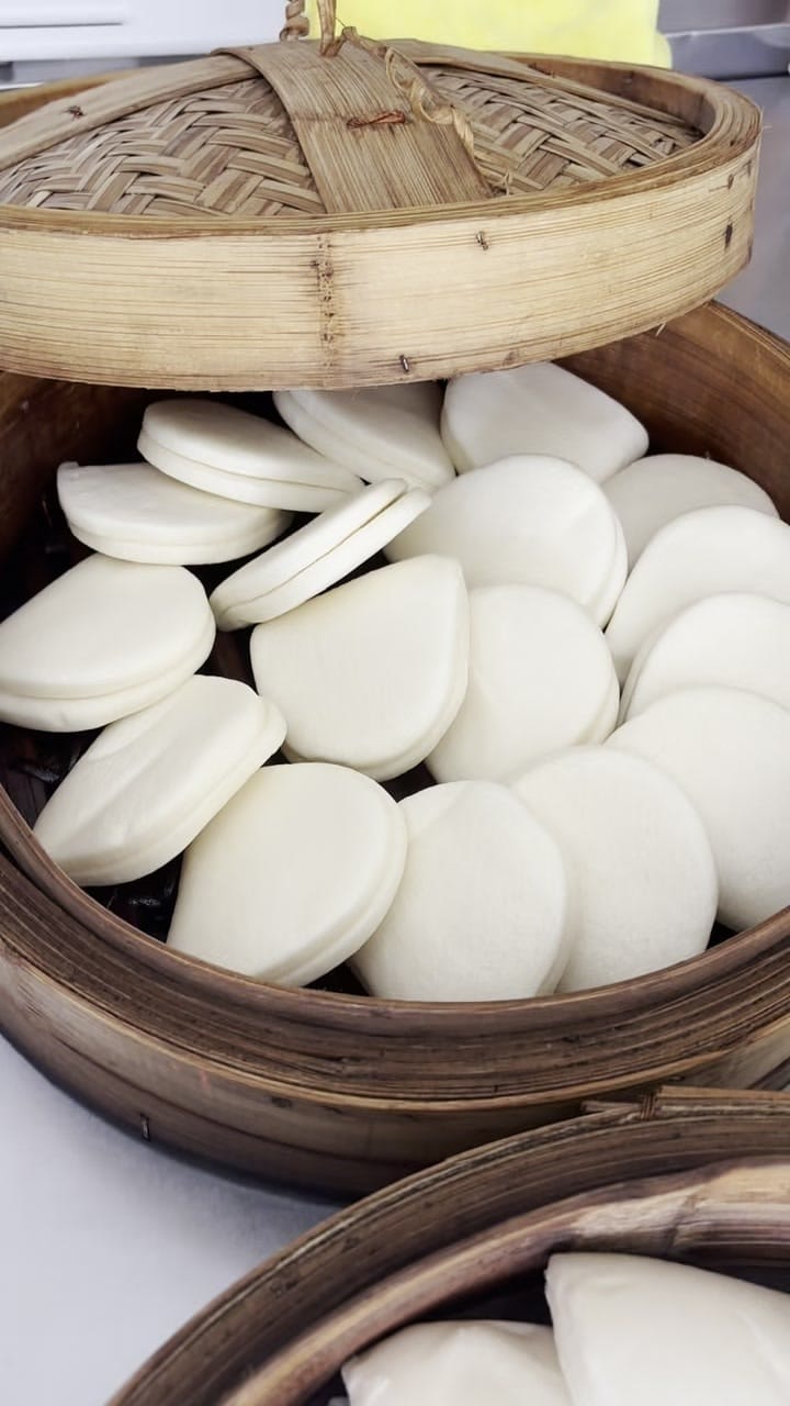 Raw bao buns resting in a stacked bamboo steamer